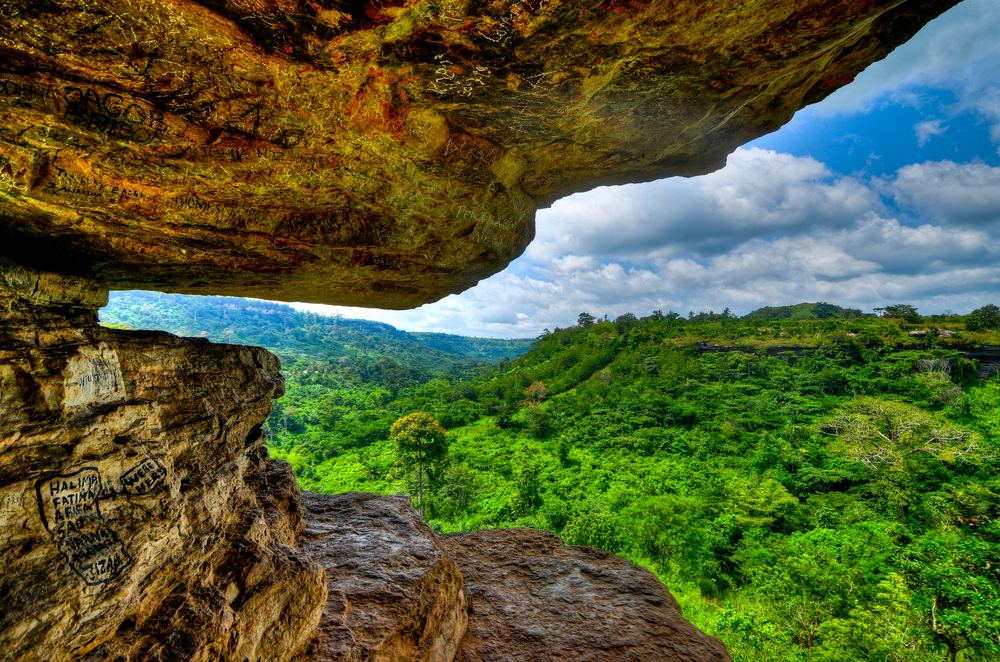 Photo of Umbrella Rock pictured from a person sandwiched between the layers with green forest below, taken during the best time to go to Ghana