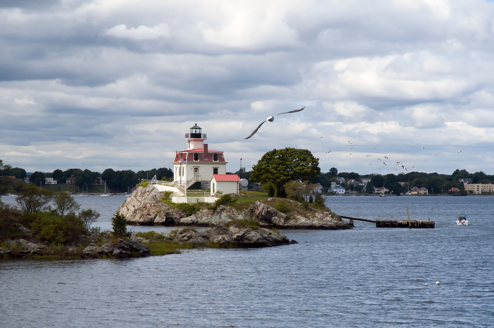 View of the Pomham Rocks Light lighthouse on a cloudy day with bird in flight over northern Narragansett Bay as one of the best places to stay in Newport RI