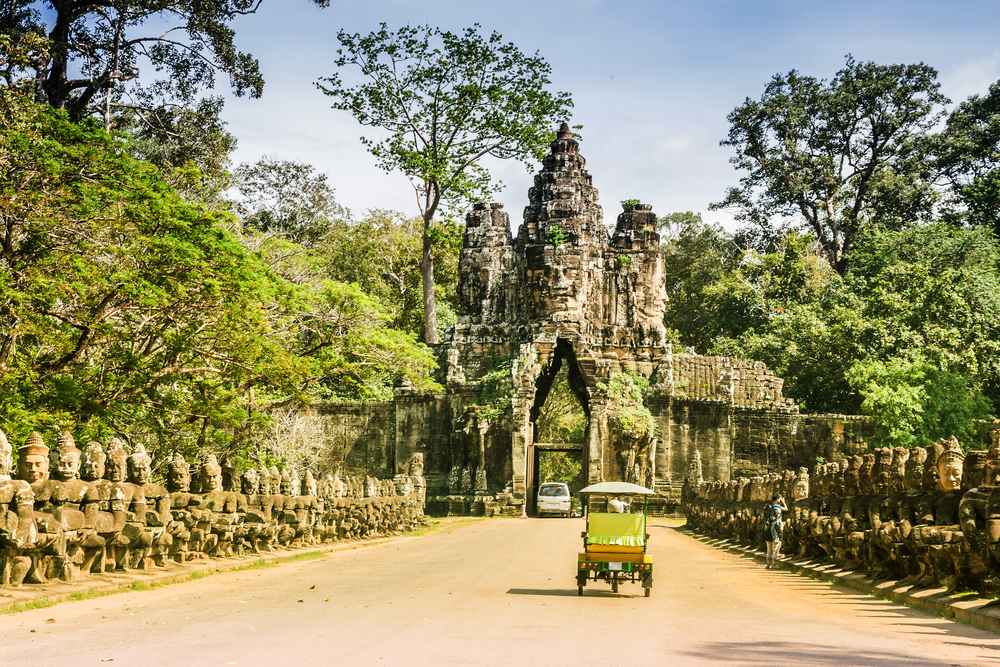The Bayon Siem Reap pictured during the best time to visit Cambodia with a tuktuk driving on a dirt road toward it