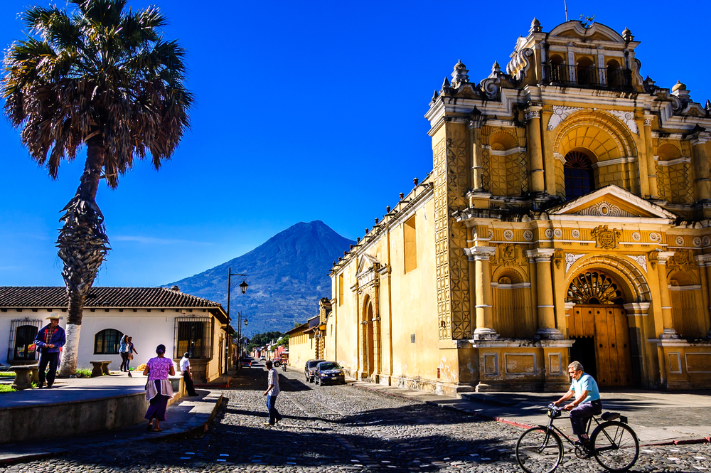 Hermano Pedro church in Antigua, Guatemala pictured during the best time to visit with blue skies in the background and vibrant locals scurrying about