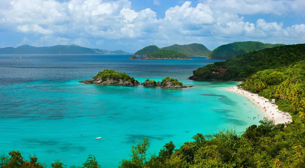Picturesque aerial view of Trunk Bay in St. John pictured with a few clouds in the sky and the world-famous white sand beaches and light turquoise water in view on the left