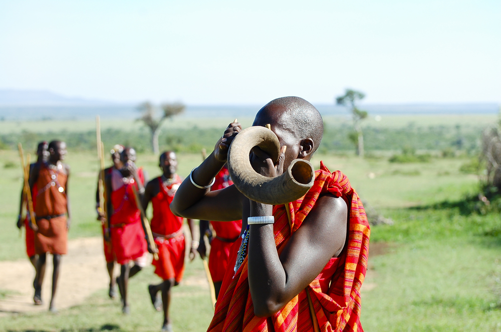 Guy in traditional tribal dress pictured during the best time to visit Kenya blowing into a Masai Kudu horn