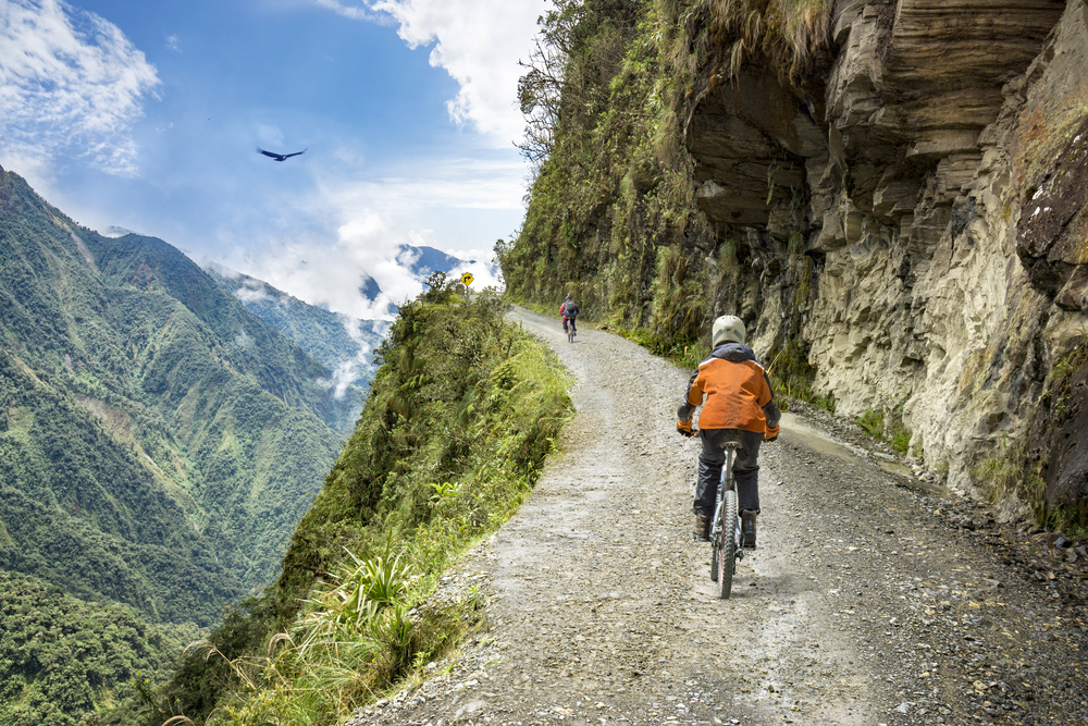 Bicyclist races down the Road of Death downhill track as birds fly during the cheapest time to visit Bolivia