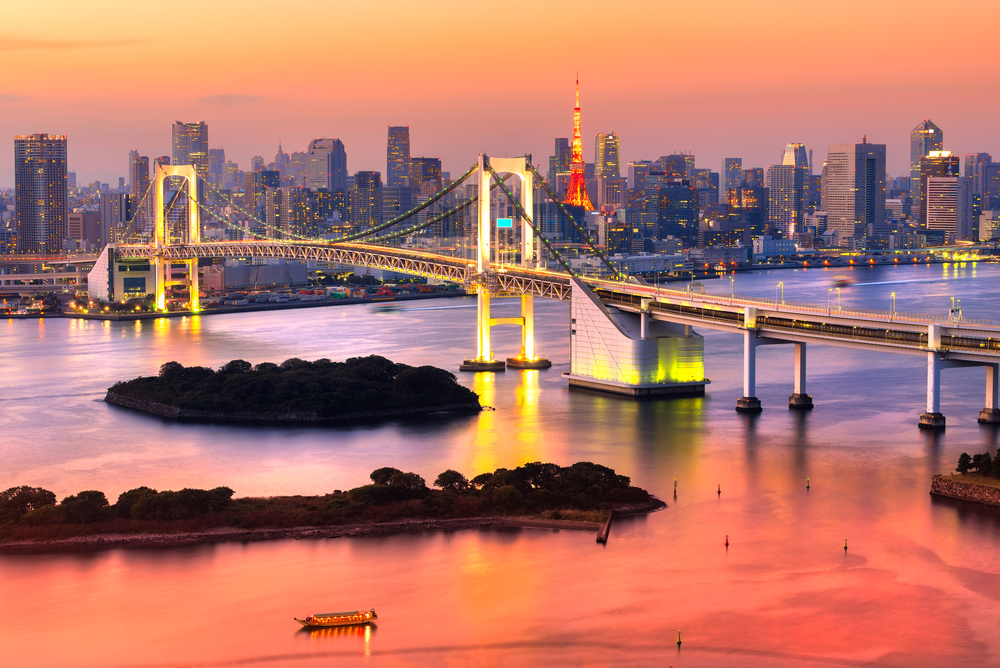 Tokyo skyline at sunset with lit bridge in view over the water