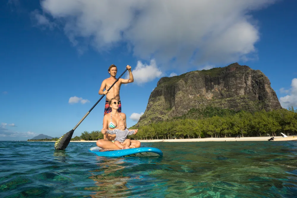Attractive blonde couple in Mauritius sitting with their child on a paddleboard