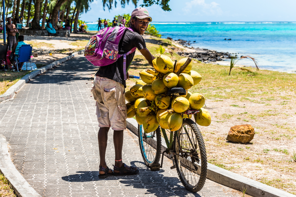 Smiling guy with a banana bike pushing his wares on a brick boardwalk along the coast of Blue Bay in Mauritius
