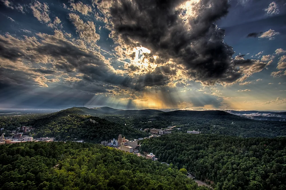 Sun rays beaming through clouds over a wide aerial view of Hot Springs during the worst time to visit Arkansas
