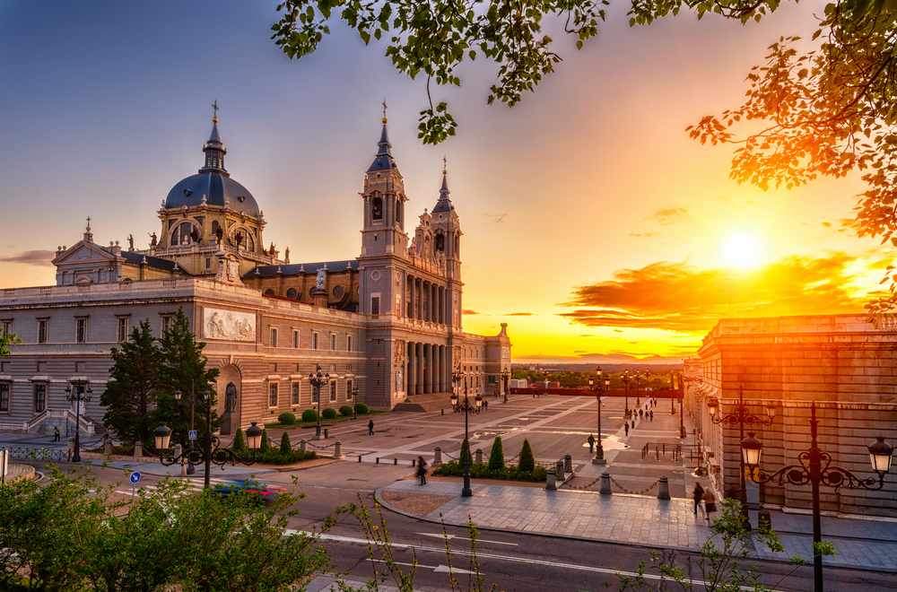 Dusk view of the Cathedral Santa Maria la Real de La Almudena pictured from the top of a tree overlooking the courtyard during the best time to visit Madrid Spain