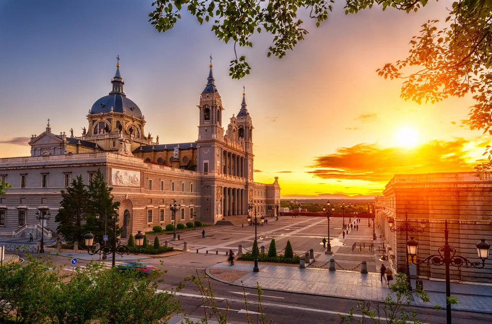 Dusk view of the Cathedral Santa Maria la Real de La Almudena pictured from the top of a tree overlooking the courtyard during the best time to visit Madrid Spain