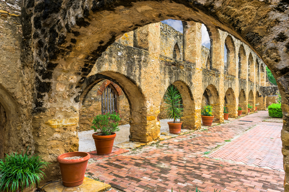Neat and artistic view of the Mission's walls during the best time to visit San Antonio with a brick path next to the planters and the walls