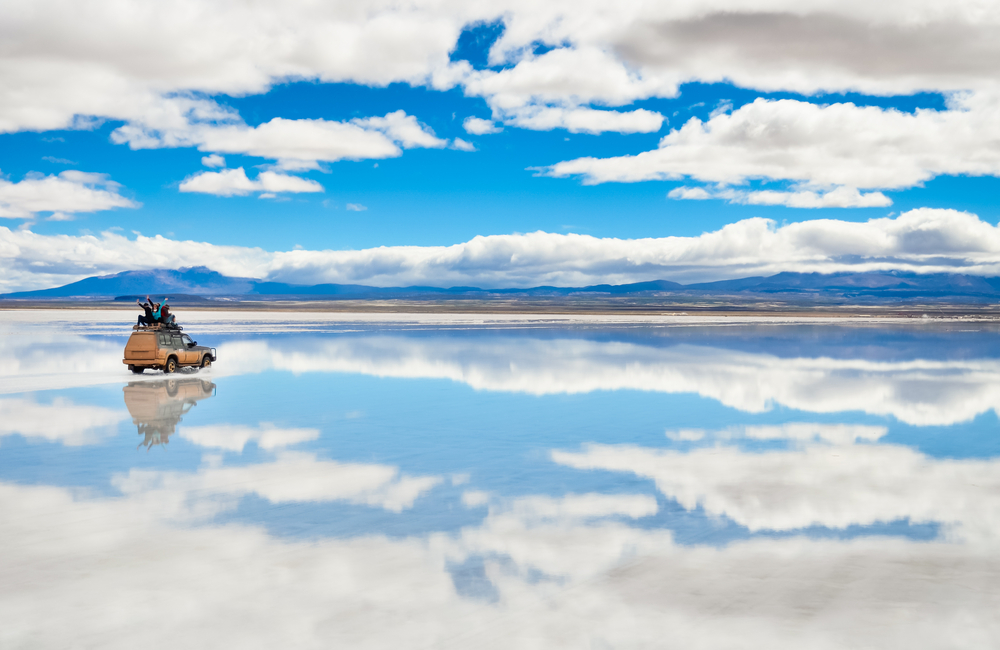 Salar de Uyuni salt flats reflecting clouds and sky with a car parked for a frequently asked questions section on the best time to visit Bolivia