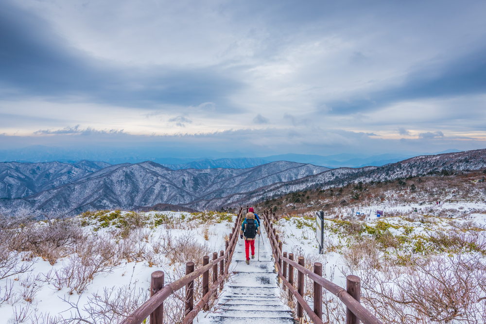 Hikers walking along snow-covered path with mountains in the distance during the worst time to visit Seoul