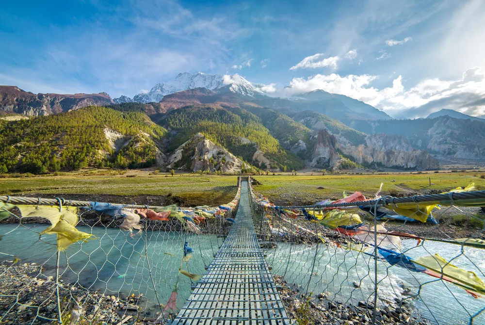 Suspension bridge leading to the Annapurna Circuit Trek pictured with prayer flags on the sides during the overall best time to go to Nepal