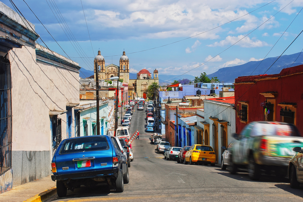 A lonely street with cars on either side pictured during a clear day during the best time to visit Oaxaca
