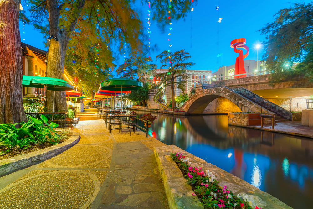 Cool night view of the riverwalk with a cobblestone and concrete path next to the water pictured during the least busy time to visit San Antonio