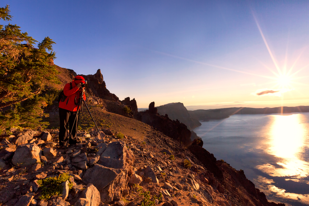 Man photographing a sunrise over Crater Lake in Oregon during the best time to visit