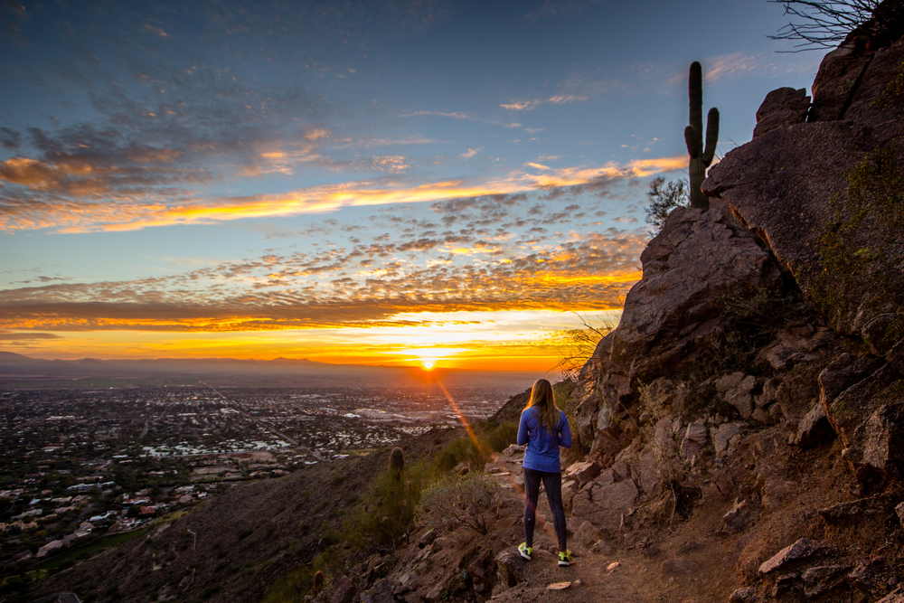 Girl watching the sunrise from the side of a mountain during the best time to visit Phoenix