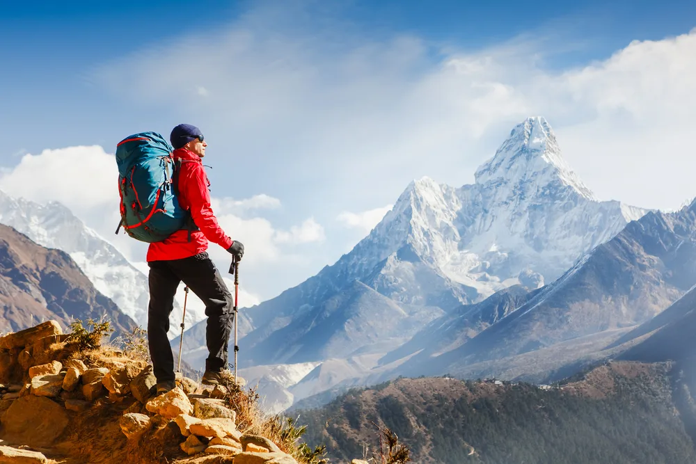 Active hiker with a backpack pictured standing on the top of a mountain looking out over the Himalayas during the best time to visit Nepal