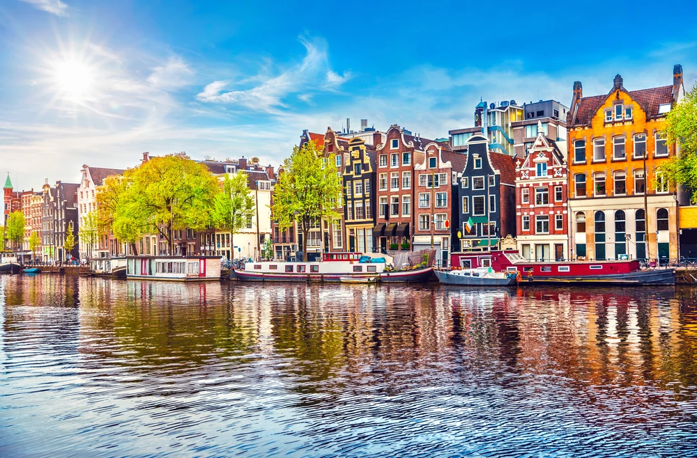 Image of Amsterdam pictured from across the river with neat old buildings in various colors pictured in the middle of Autumn, the best time to visit the Netherlands