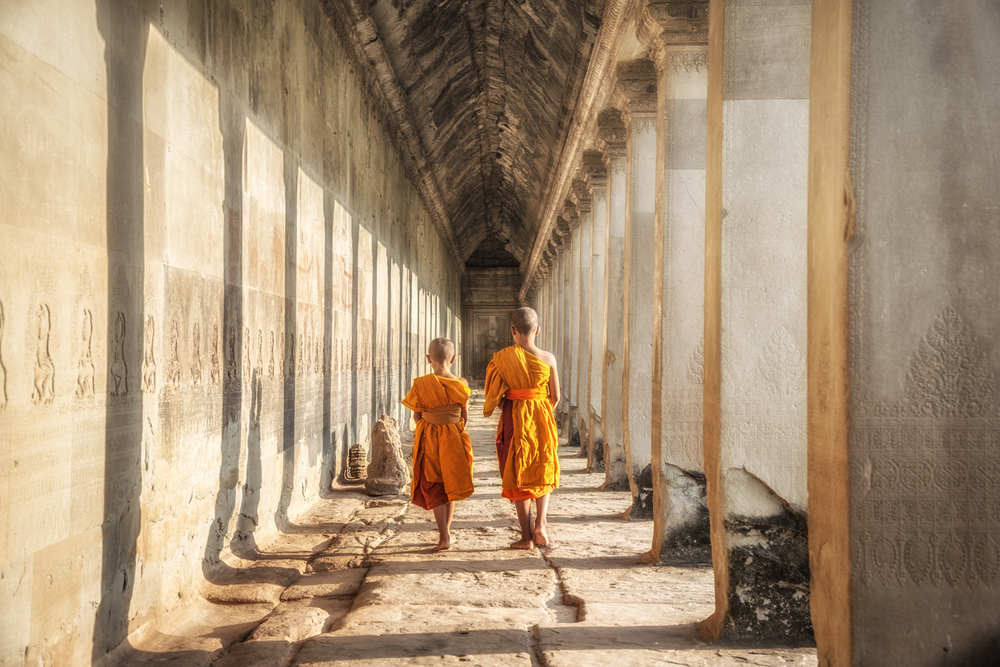 Two monks in orange robes walking down the stone temple walkway in Cambodia
