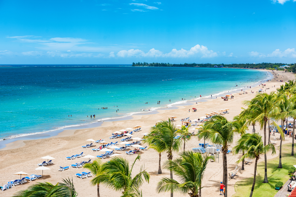 Long stretch of tourist beach with chairs and palm trees pictured during the Spring, the overall best time to visit Puerto Rico