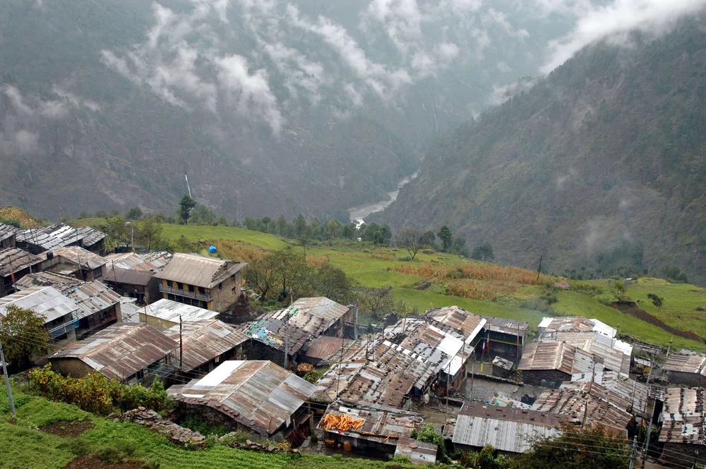 Tin roofs held down with rocks pictured on the side of a large mountain during the worst time to visit Nepal