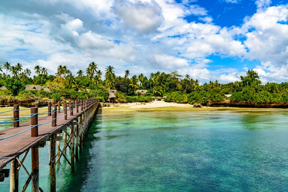 Beach on the Zanzibar Coast as seen from a dock during the best time to visit Tanzania with clouds obstructing the hot sun and clear teal water