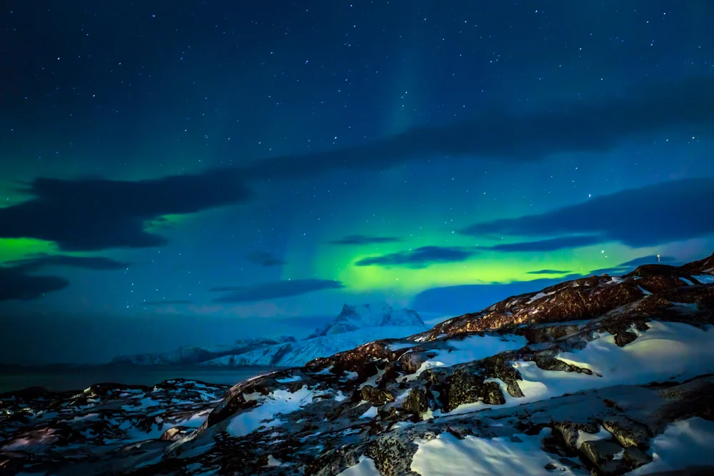 Photo of the northern lights shone in green color high above the mountain during the cheapest time to visit Greenland