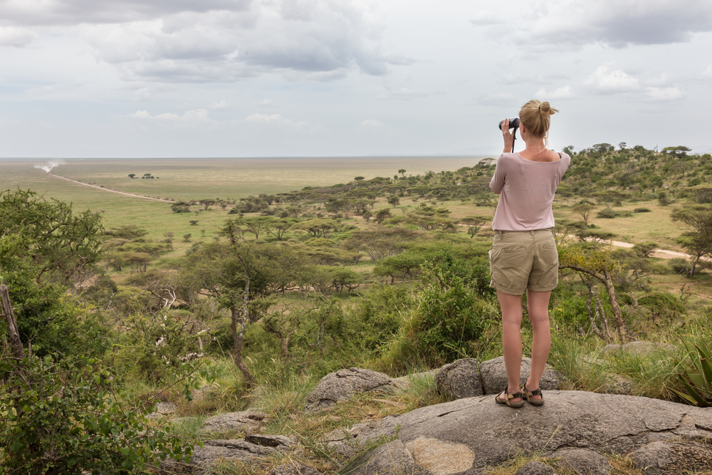 Woman looking through a pair of binoculars over an expansive forest during the best time to visit Tanzania