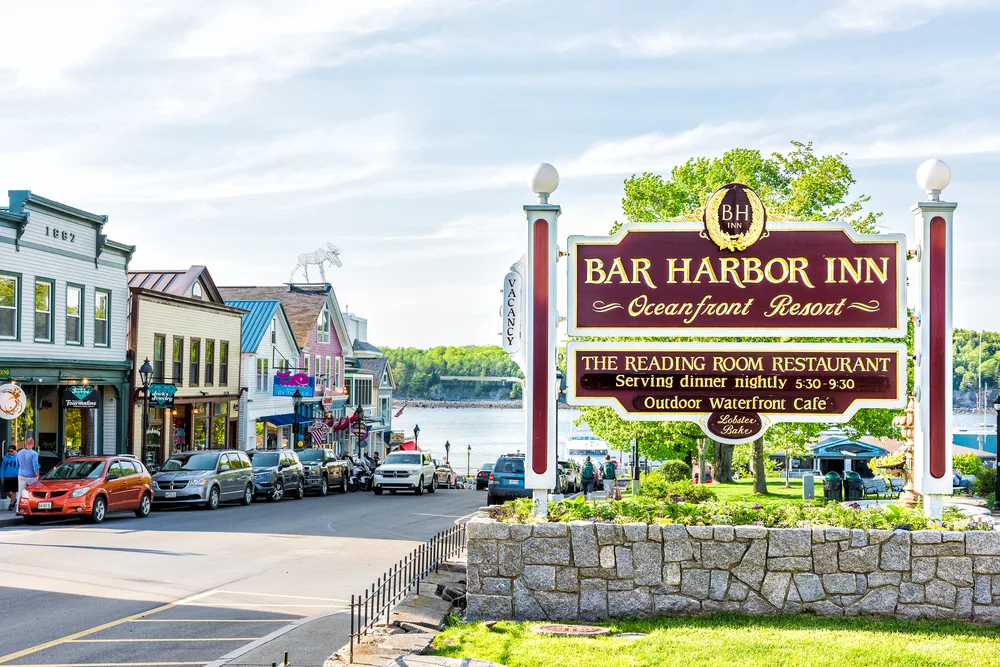 Photo of the oceanfront resort Bar Harbor Inn pictured on a nice summer day under semi-cloudy but blue skies with the downtown area pictured in the foreground during the best time to visit Bar Harbor