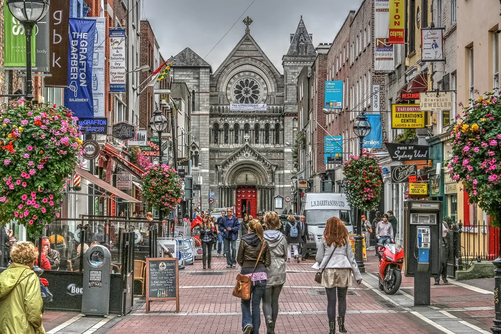 Many pedestrians walking along a brick pathway between big buildings as seen during the best time to go to Dublin