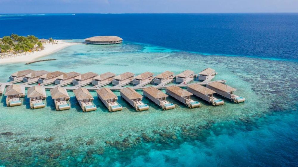 Neat view of the bungalows at Kagi Maldives Spa Island, one of the best resorts in the Maldives, with gorgeous teal water below a blue sky