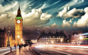 As a featured image for a piece on the best day trips from London, Big Ben towers over the road below with cars and people making their way bay and storm clouds overhead, as seen at night