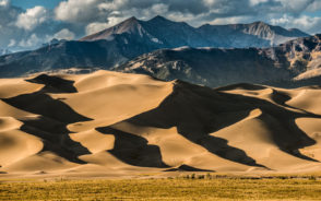 Featured image depicting the best time to visit the Great Sand Dunes National Park with rolling hills of sand in the foreground and snow-capped mountains in the back
