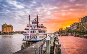 Riverboat on the riverfront promenade pictured at sunset with an orange sky in the background for a piece on the best places to visit in Georgia
