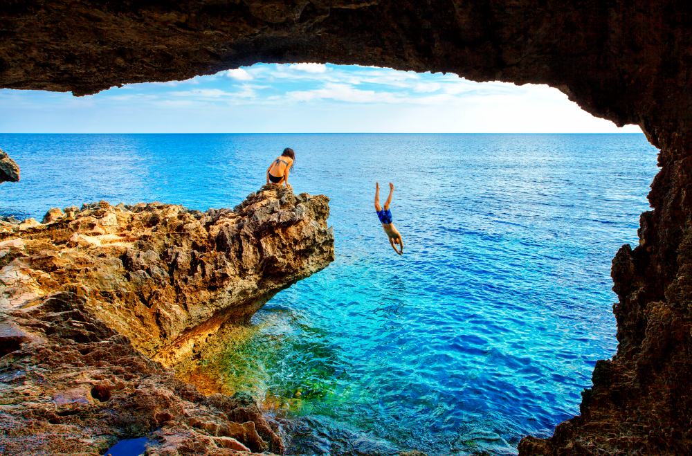 Guy in blue shorts diving into the ocean from a big rock pictured during the cheapest time to visit Cyprus