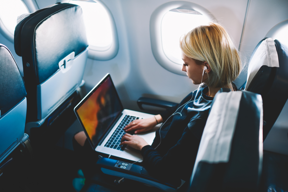 Woman using laptop on airplane to show when to buy travel insurance during your trip