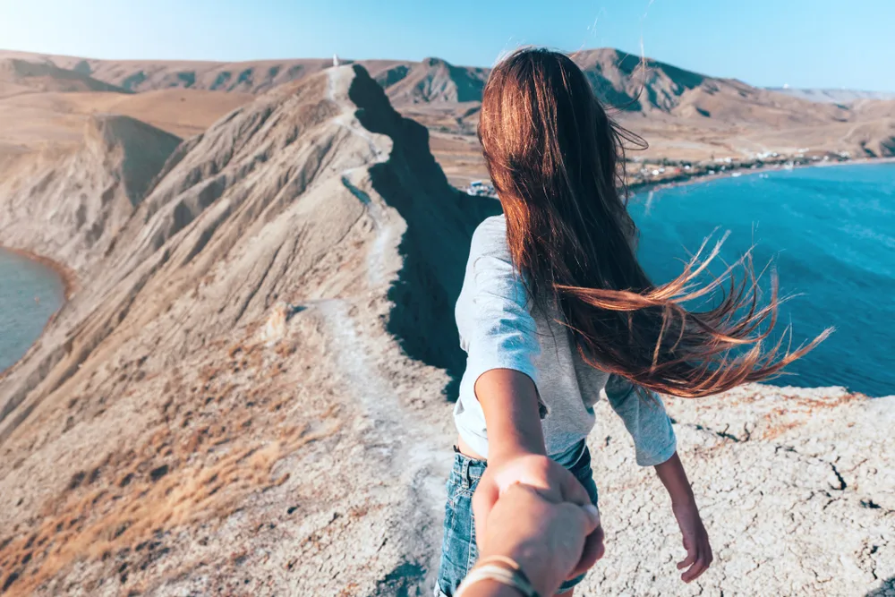 Girl walking on a mountain while holding the hand of the cameraman for a piece on the best wanderlust quotes
