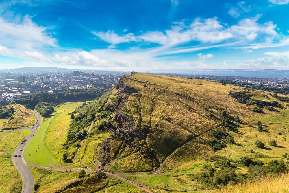 Aerial view of Arthur's Seat, one of the best places to visit in Scotland, seen overlooking the city on a blue sky day