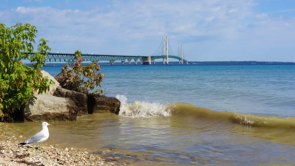 Bridge spanning Lake Huron with waves lapping the rocks on the shoreline during the best time to visit Mackinac Island