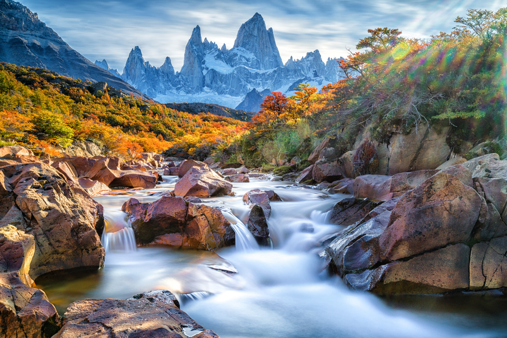 Fitz Roy Mountain in a stunning image behind a waterfall with misty water between rocks pictured for a piece on the best places to visit in South America
