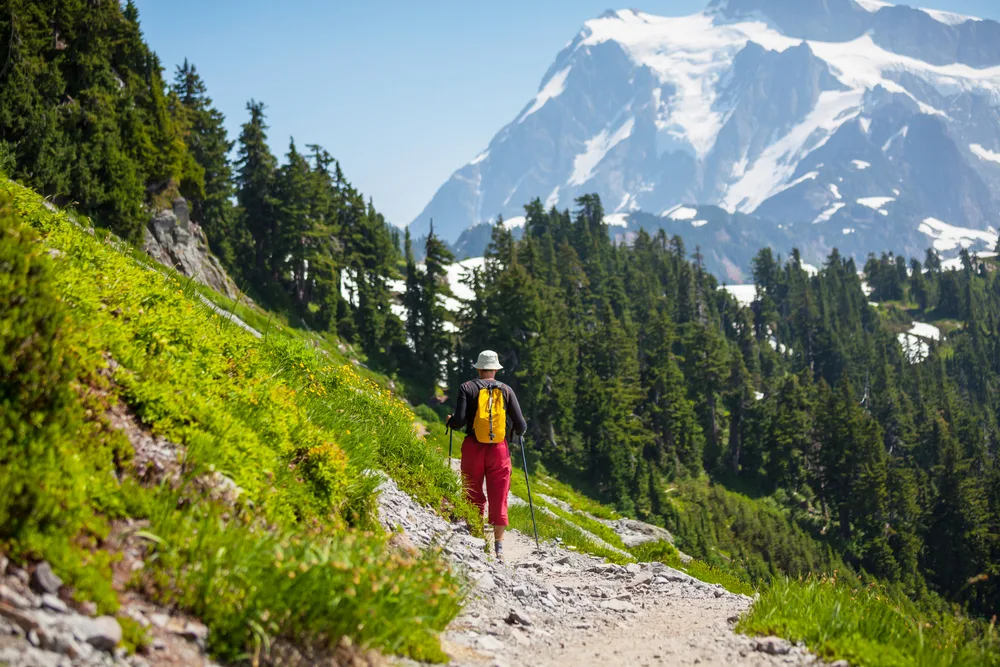 Man in a hat and red pants hiking on a cliffside trail in North Cascades National Park during the overall best time to visit