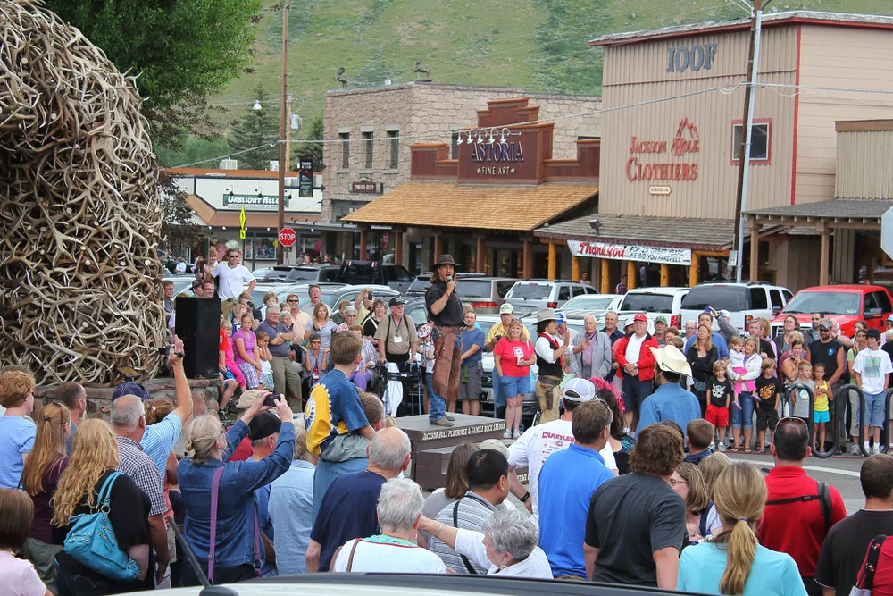 Man speaking next to a big pile of deer antlers outside with a huge crowd pictured in the summer, the worst time to visit Jackson Hole