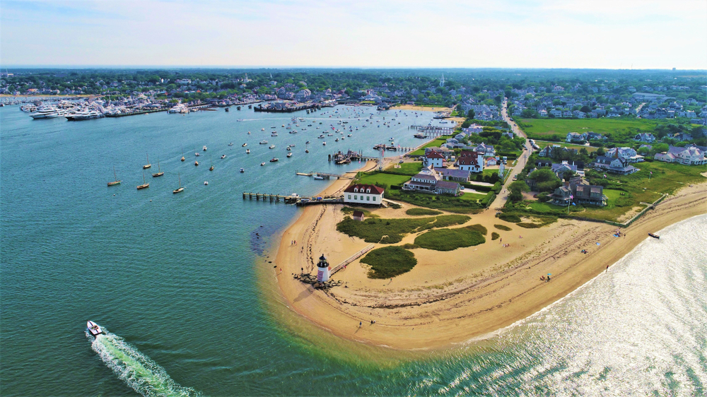Entrance to the harbor pictured from the air with a lighthouse at the tip of the beach during the best time to visit Nantucket