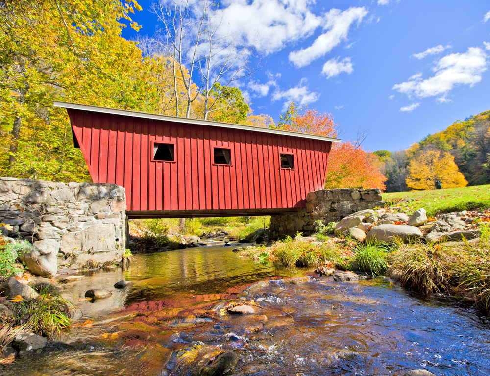 Gorgeous bridge in the fall pictured over a stream during the best time to visit New England