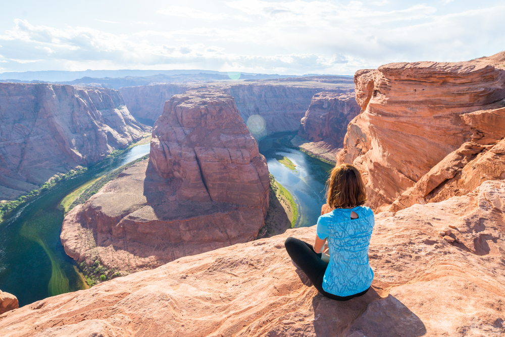 Woman sitting cross-legged on the top of a rock overlooking Horseshoe bend during the best time to visit, the morning