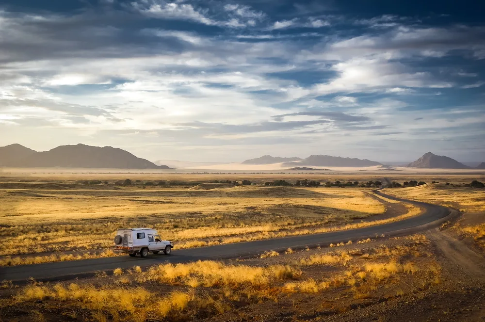 Early morning in Namibia on the way to the sand dunes with a lone truck with a camper driving along the road under a cloudy sky with haze on the horizon