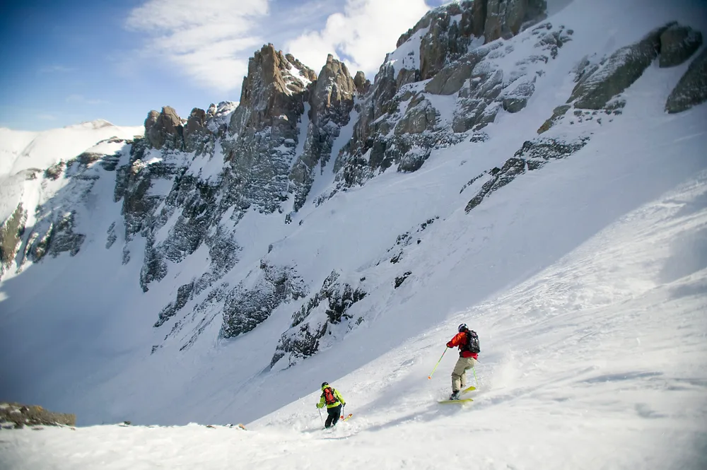 Two people skiing down Mountain Quail in yellow and red coats during the winter, the overall best time to visit Telluride
