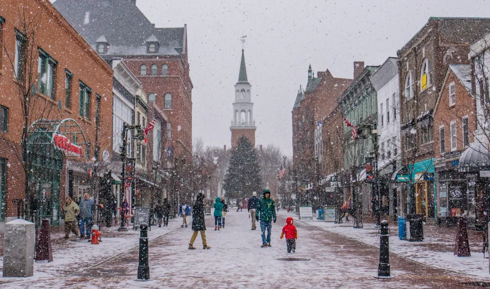 Winter in Burlington Vermont pictured with people walking all around the main street while snow falls around them on Christmas