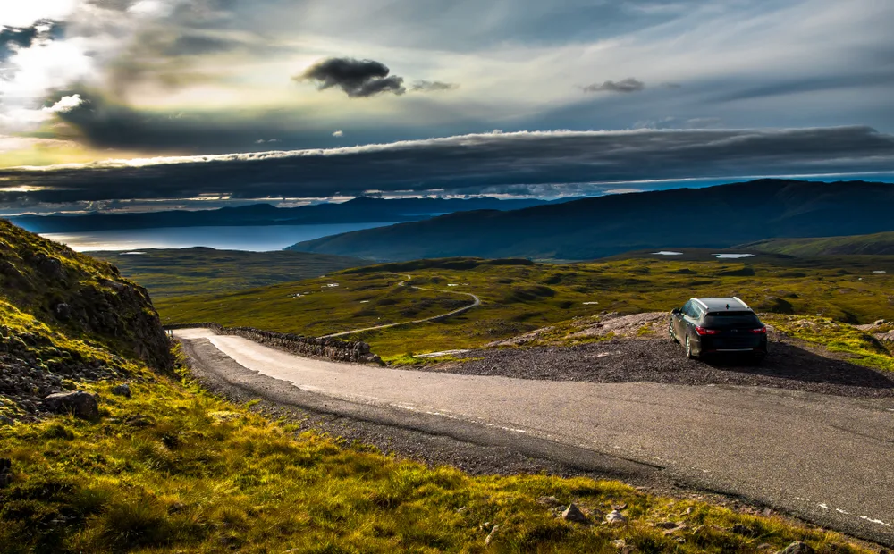 Gorgeous view of Applecross, one of the best things to do in Scotland, pictured during dusk with a parked car overlooking a big lake and hills with windy roads
